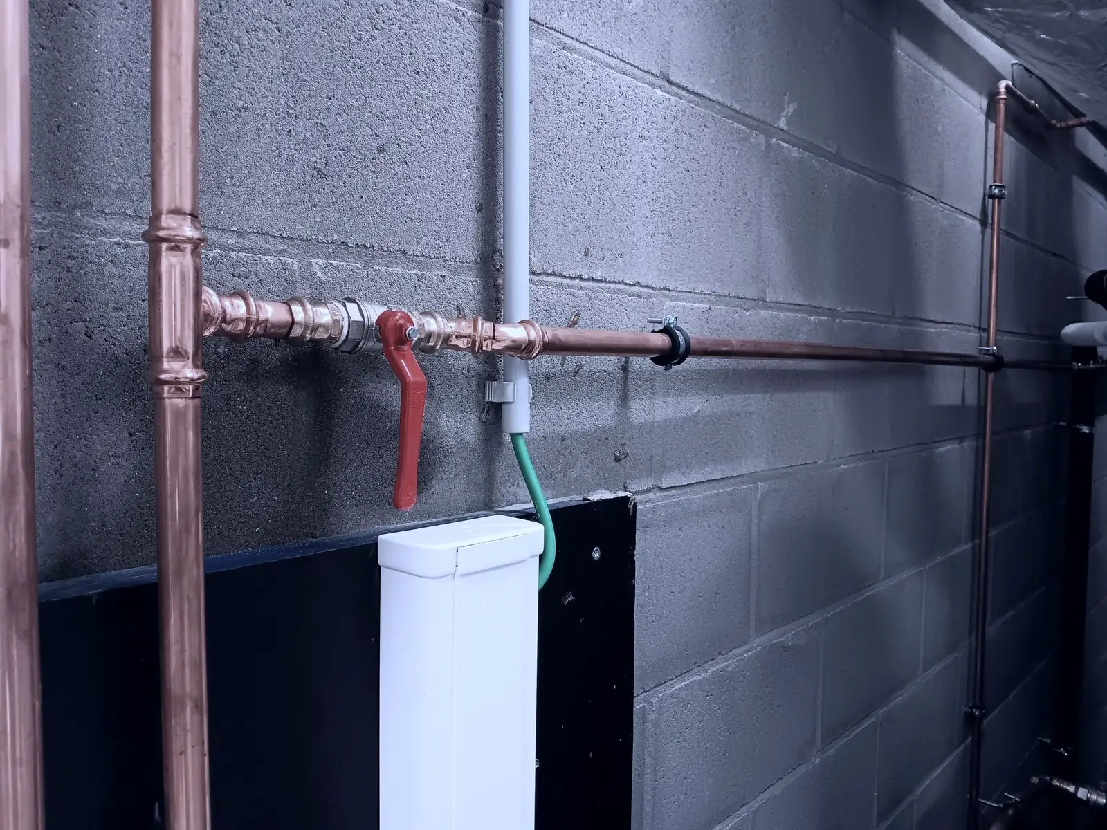 Koperen leiding met kogelkraan en aftakking langs een kelderwand